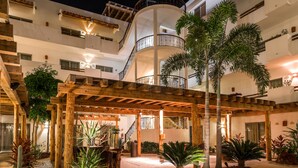 Un edificio de varios pisos con un espacio exterior cubierto que incluye vigas de madera, palmeras y una zona de estar.