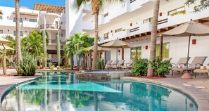 Un área de piscina con sillones de descanso y palmeras.