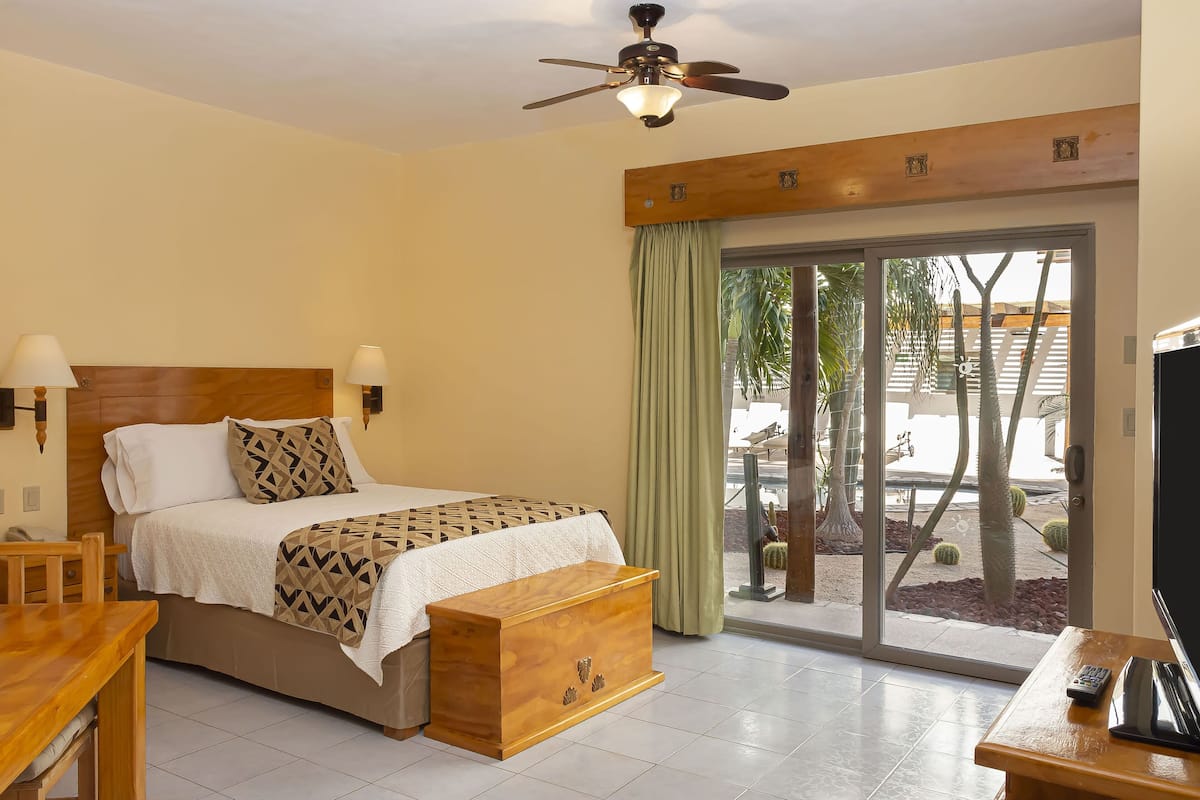 Una habitación de hotel con una cama, una mesita de noche de madera, un escritorio con un control remoto y un ventilador de techo.