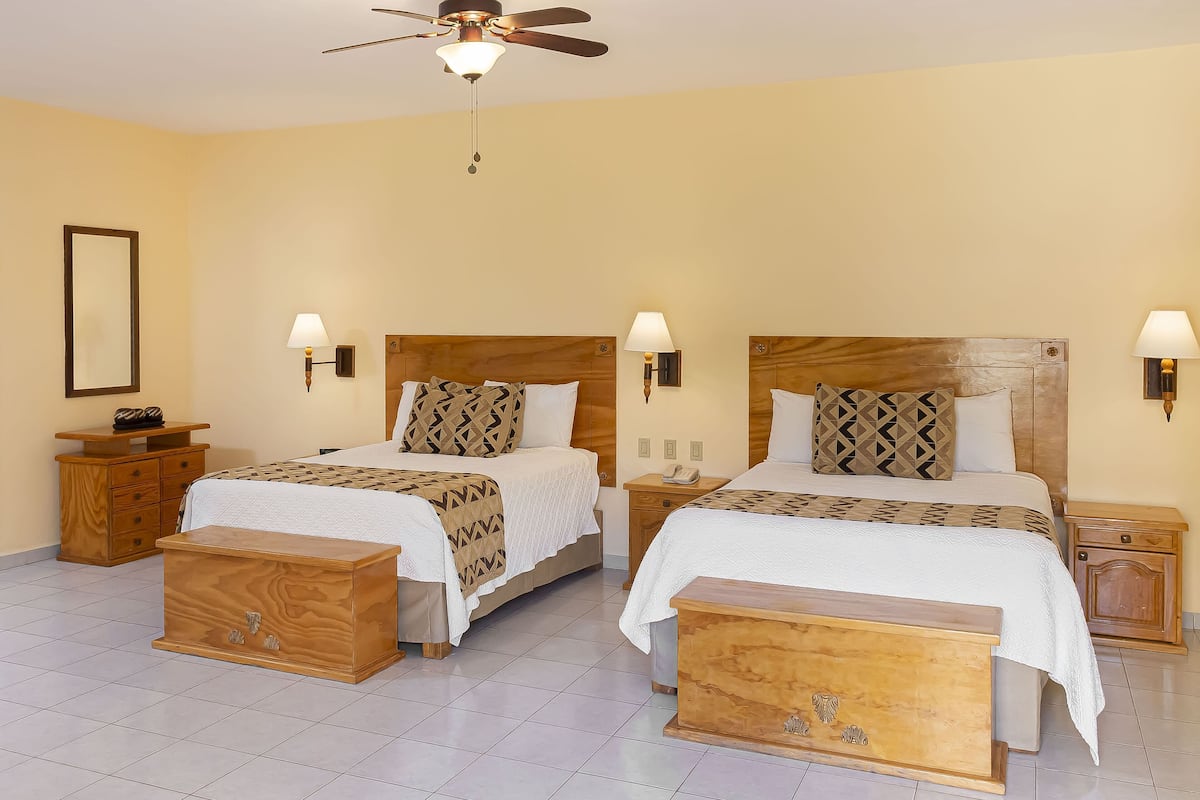 Habitación de hotel con dos camas, cabeceros de madera, mesitas de noche y un ventilador de techo.