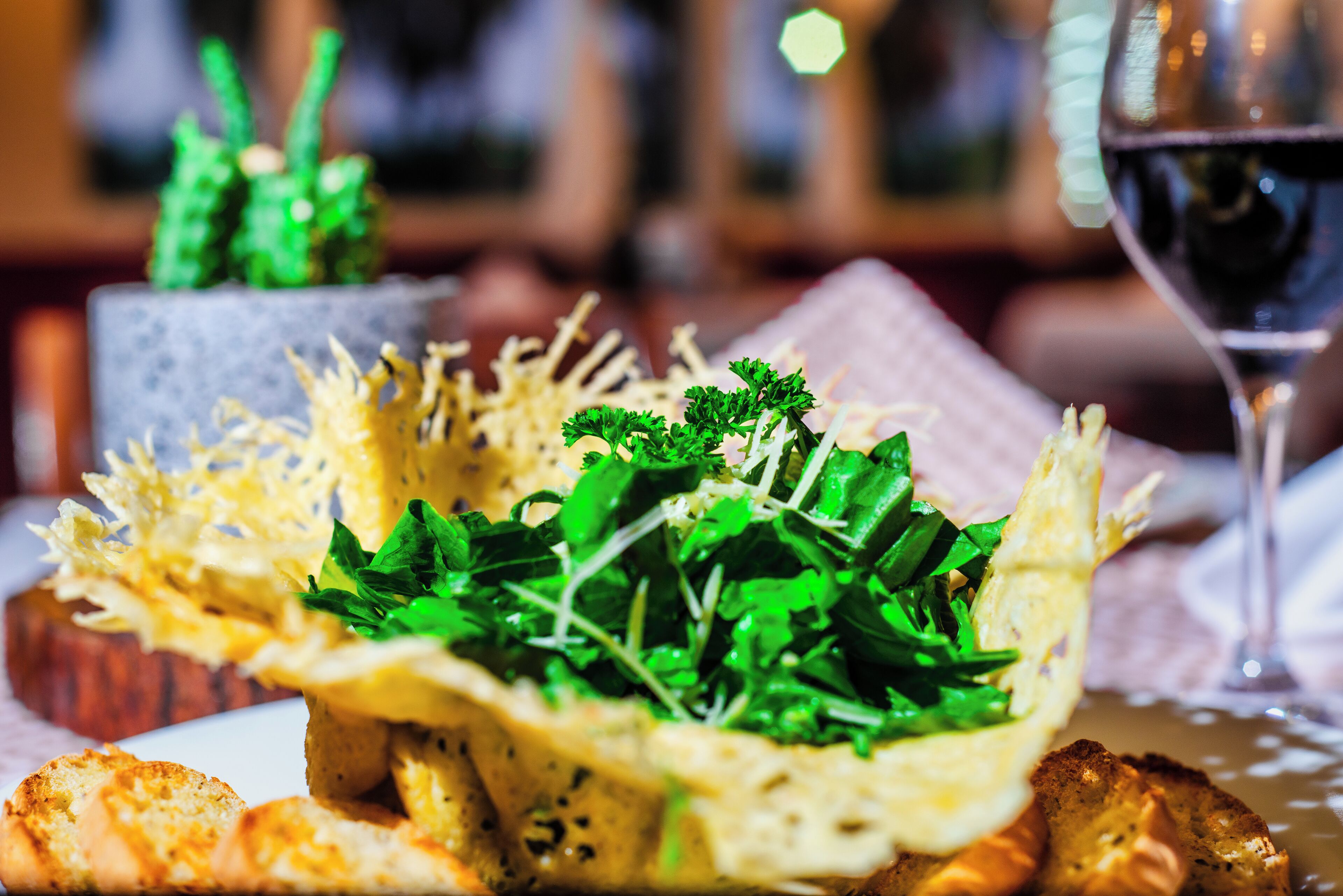 A dining table with a basket of greens and bread.