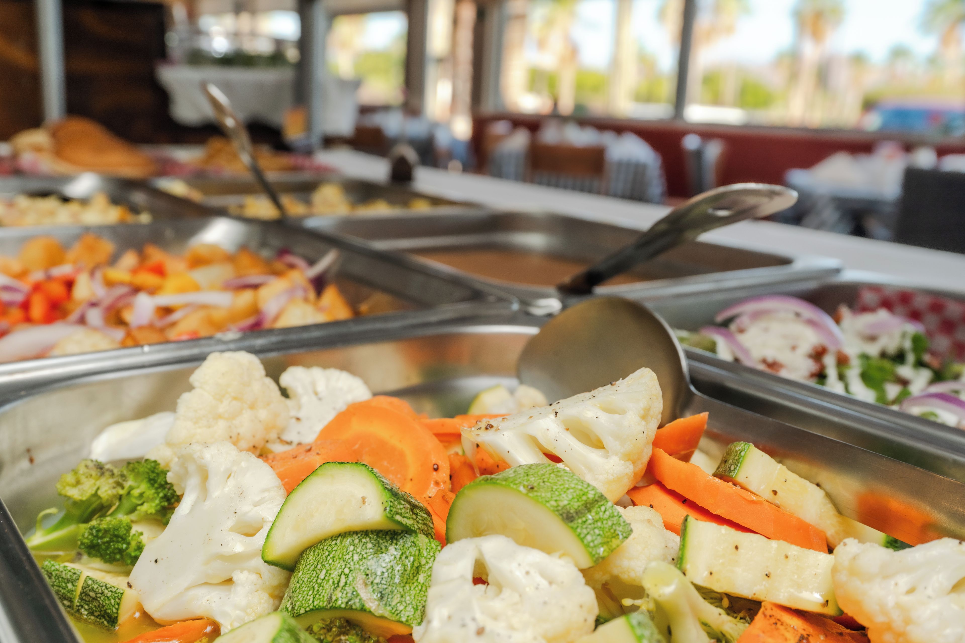 A buffet with various vegetables and a spoon on the table.
