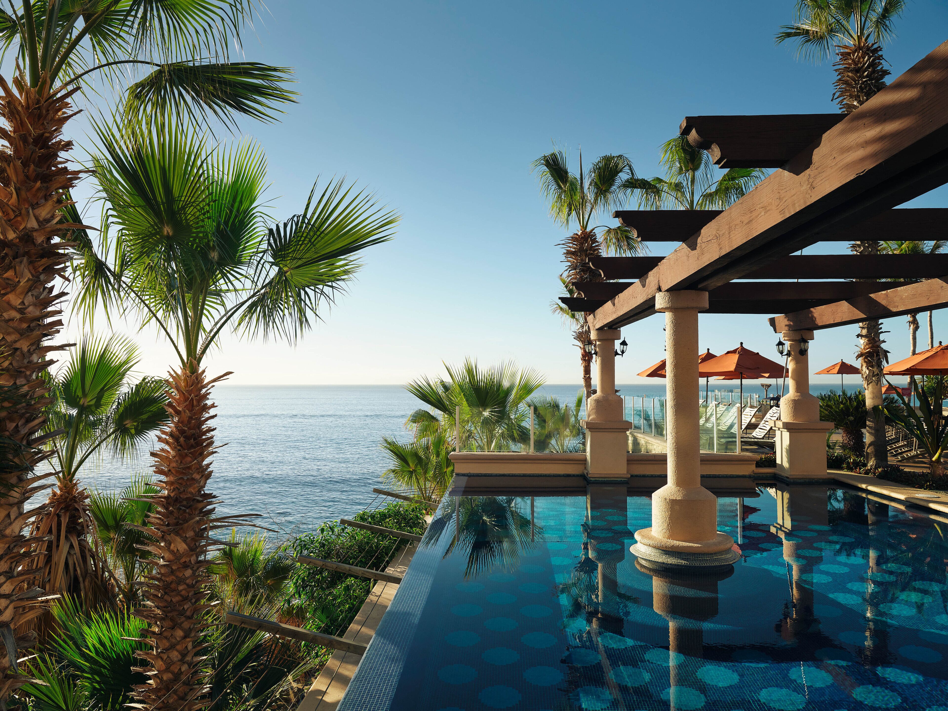 Un espace aménagé au bord de la piscine, offrant une vue sur l’océan, les palmiers et une pergola.