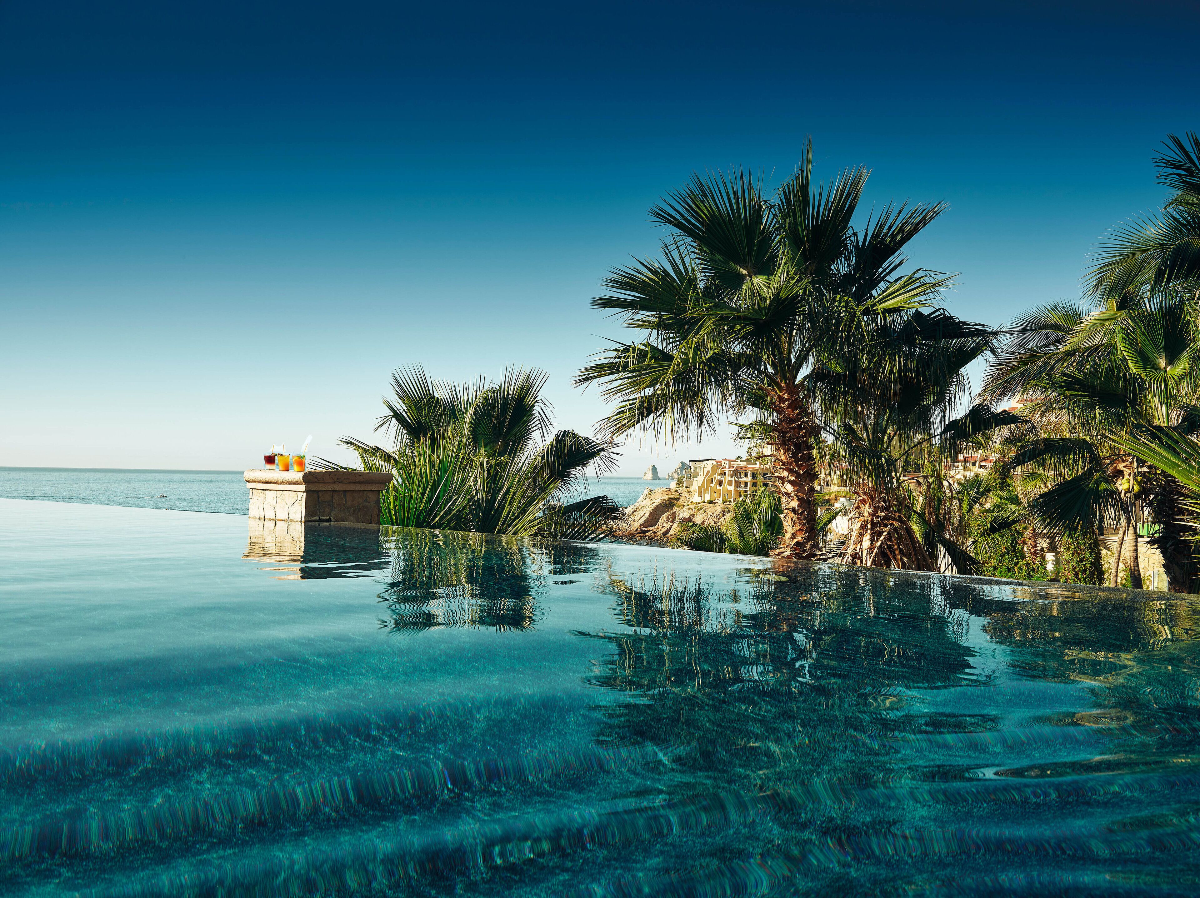 Ein Pool ohne Ende mit klarem Wasser, Palmen und Blick auf den Ozean.