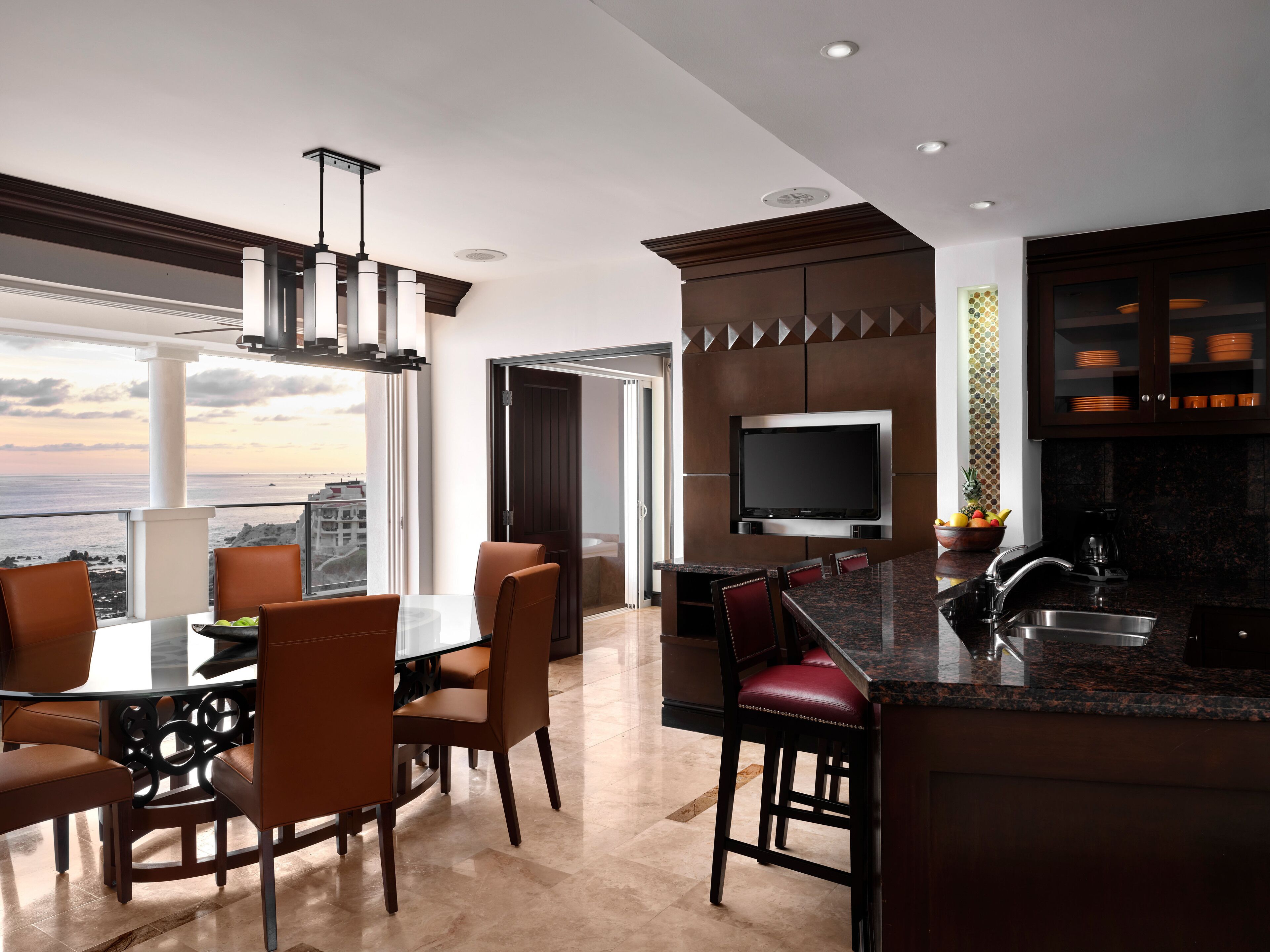 A modern kitchen with a large island, a dining area with chairs, and a view of the ocean.