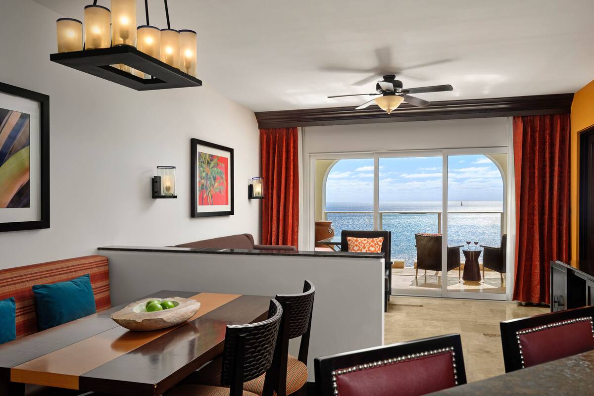 Uma zona de refeições com vista para o mar, um ventilador de teto e uma mesa com cadeiras.