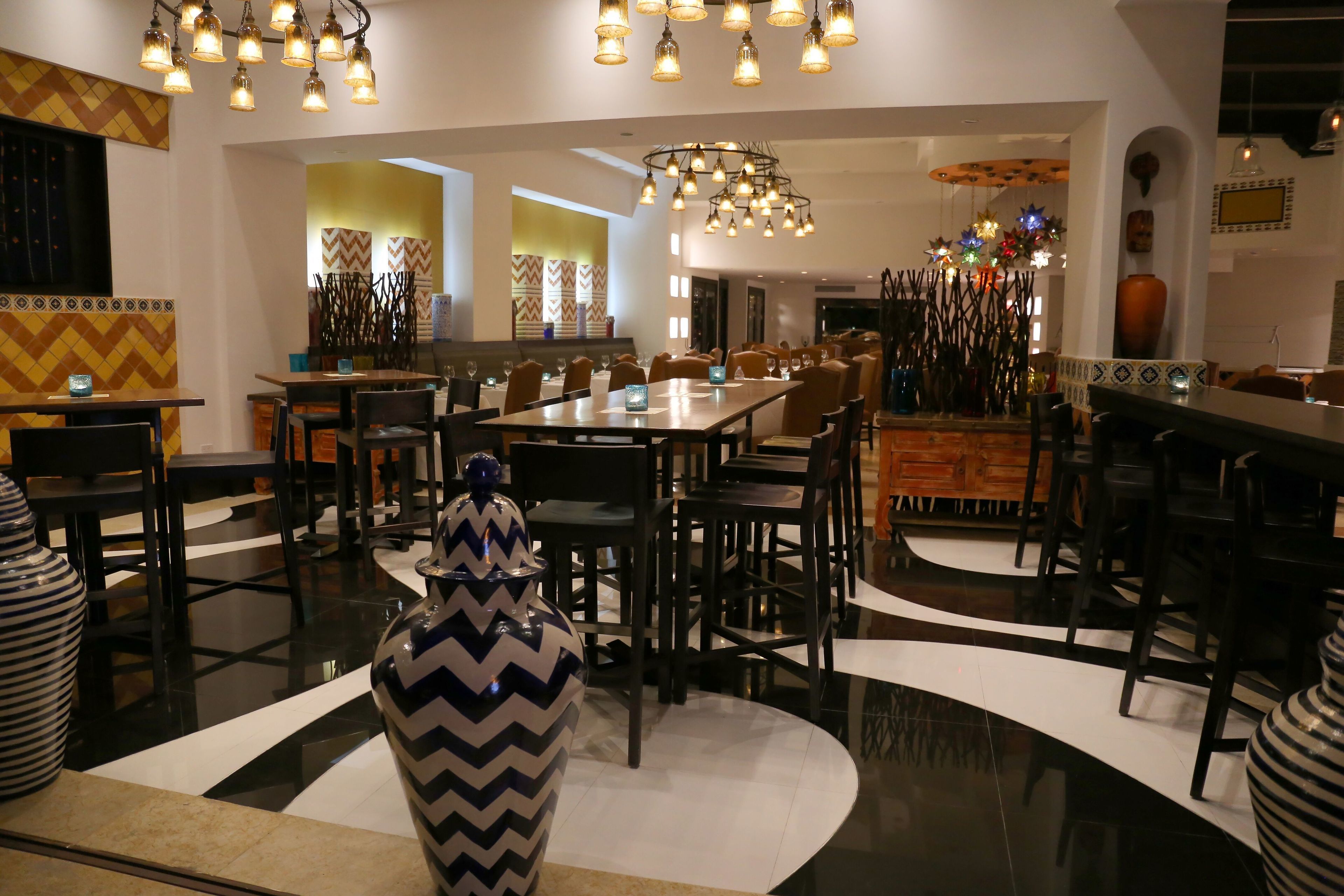A modern dining area with multiple tables and chairs, decorative vases, and a central chandelier.