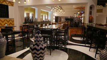 A modern dining area with multiple tables and chairs, decorative vases, and a central chandelier.