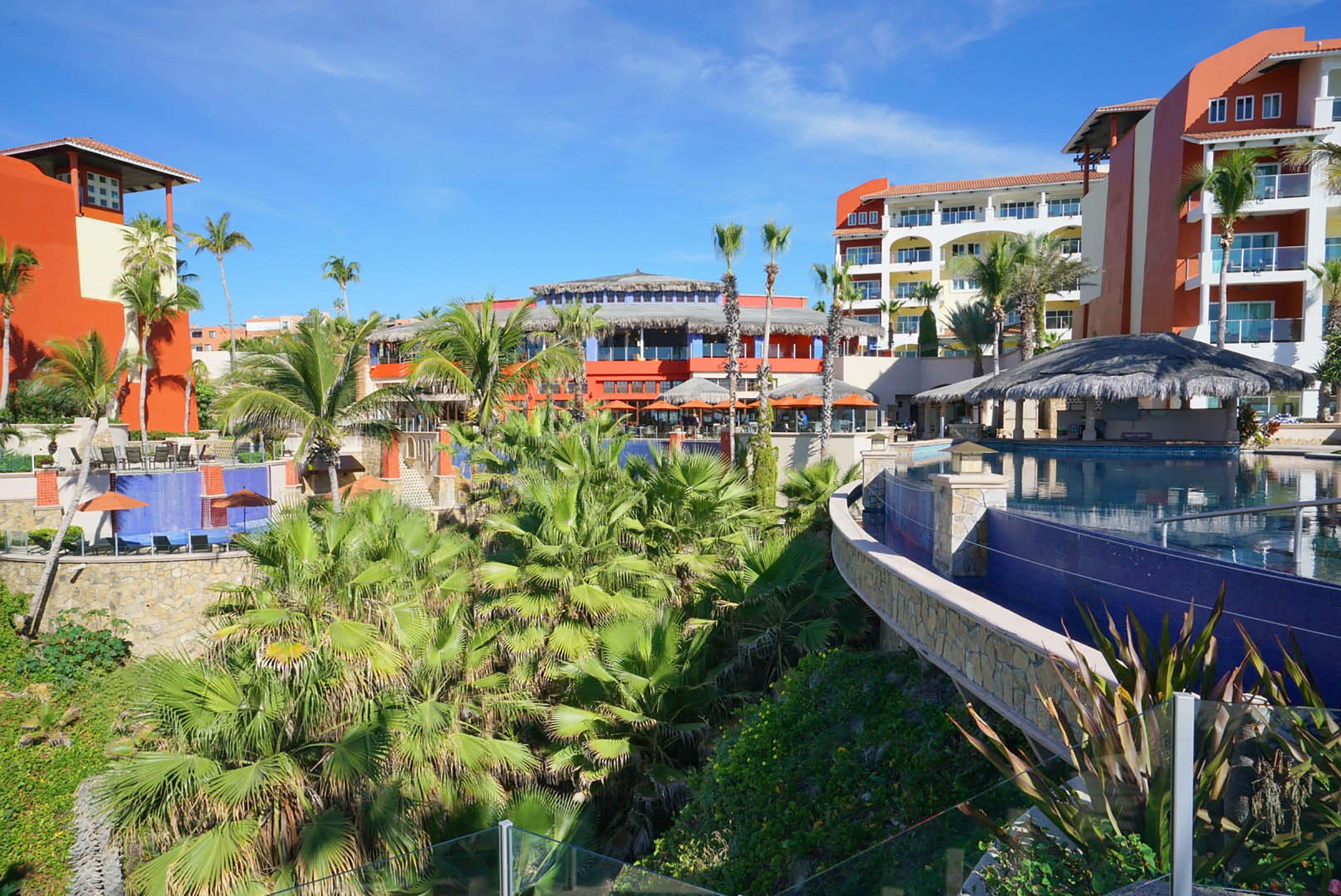 Een resort met een zwembad, palmbomen en meerdere gebouwen met balkons.