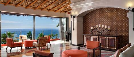 A spacious lobby with a view of the ocean, a thatched ceiling, and a patterned wall.