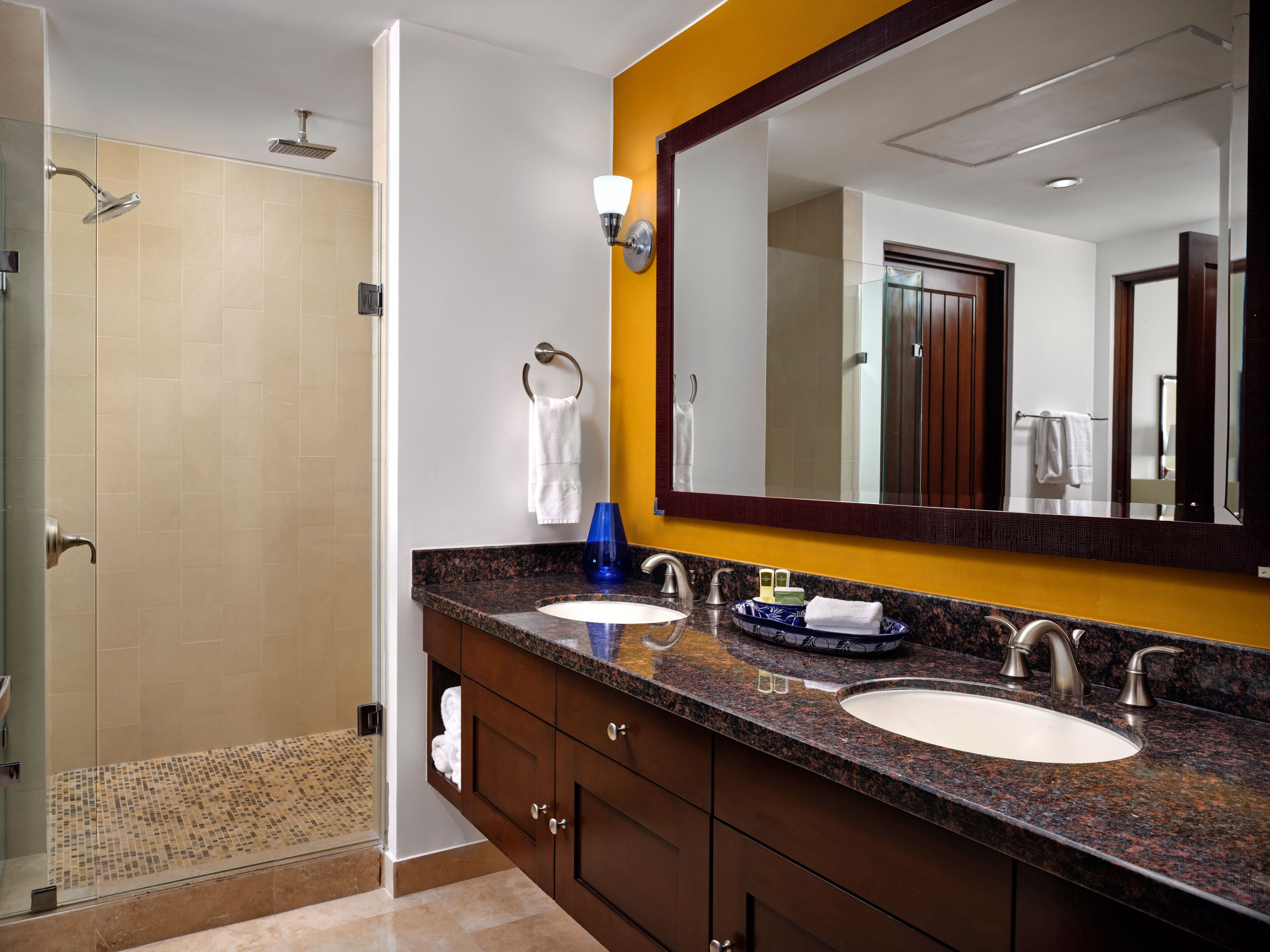 A modern bathroom with two sinks, a large mirror, and a shower area.