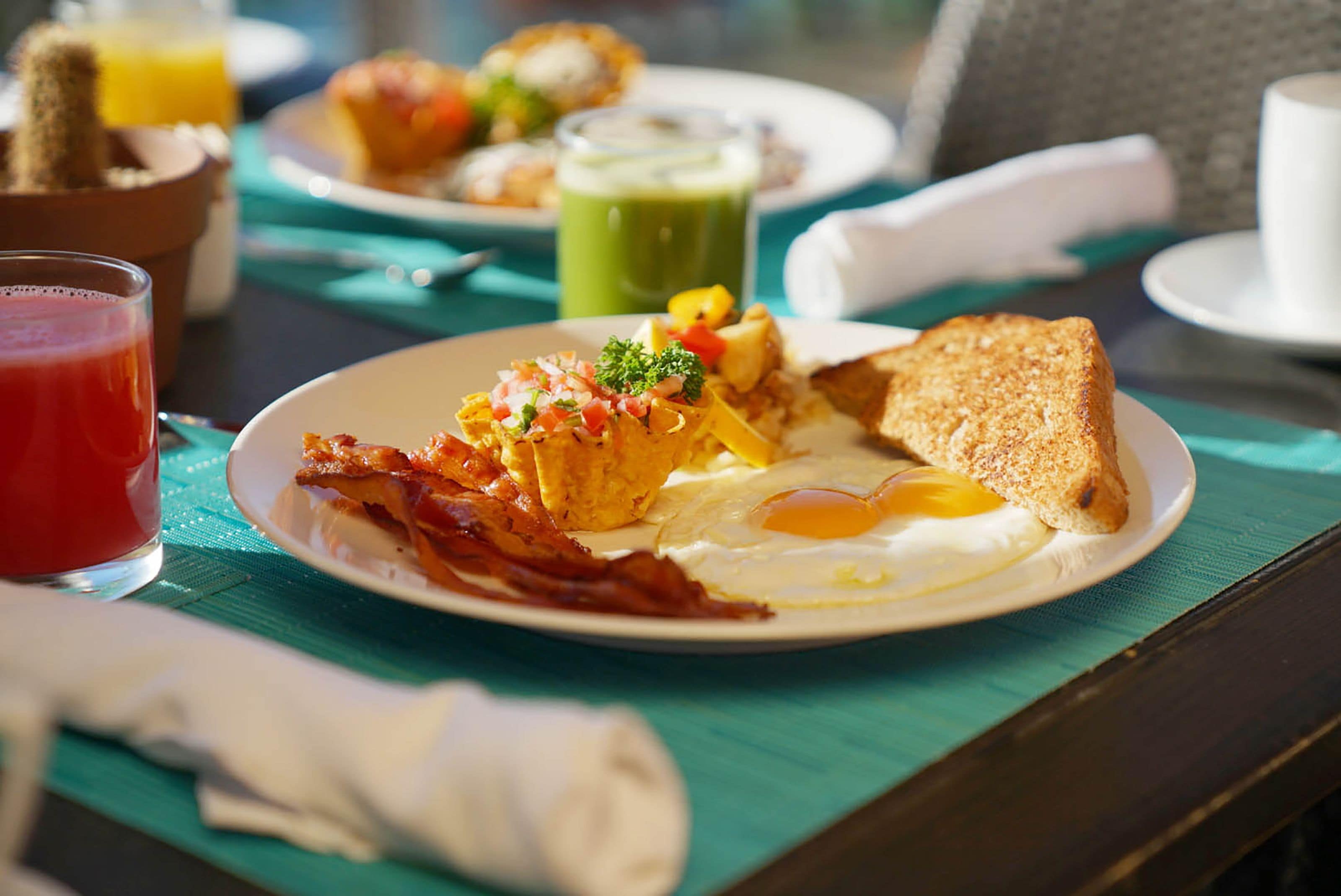 Un plato de desayuno con huevos, tocino, tostadas y una bebida verde sobre una mesa.