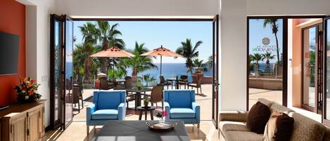 A spacious living room with a large window overlooking the ocean, furnished with blue and brown sofas, a coffee table, and two umbrellas.
