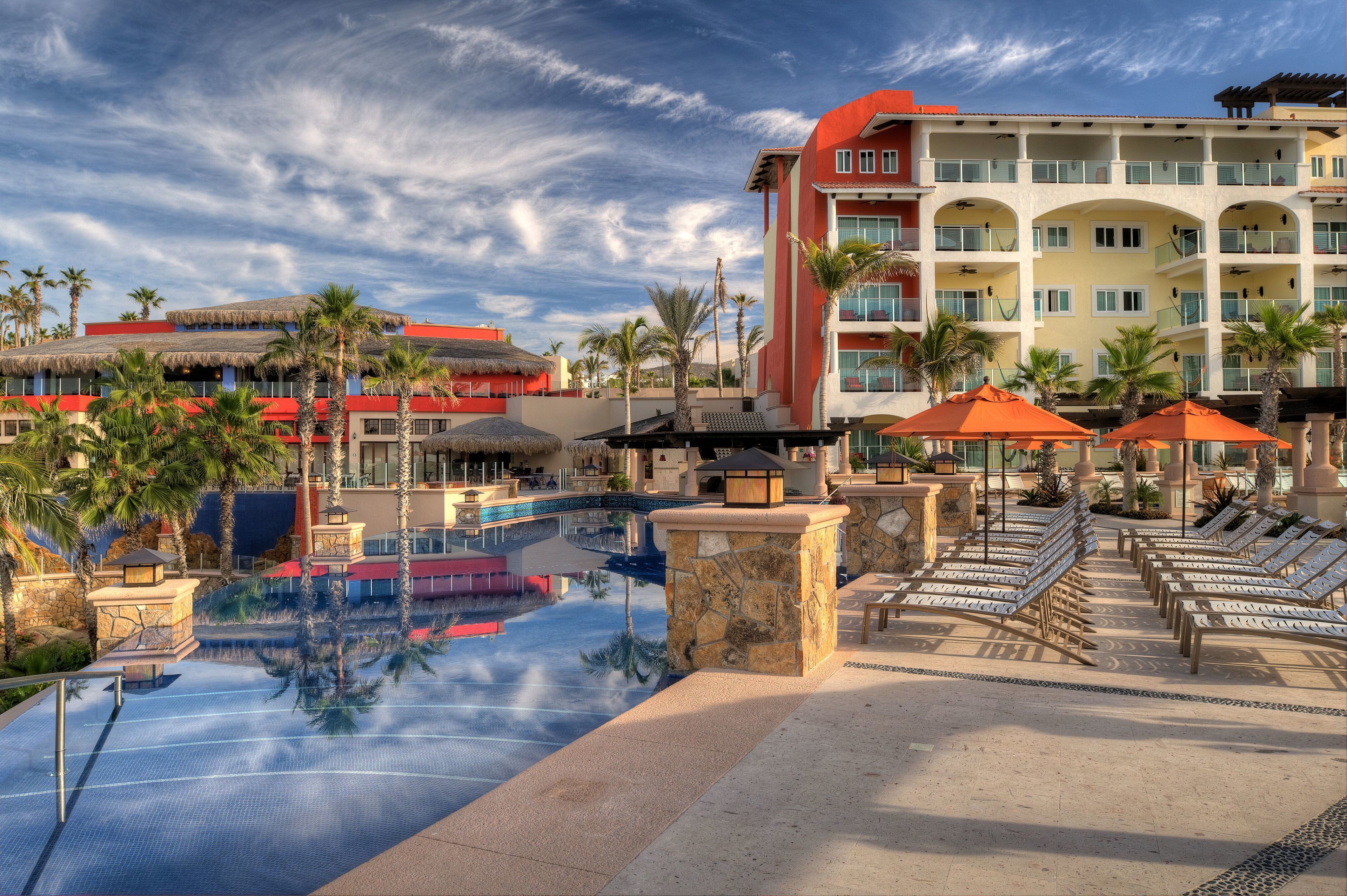 A resort with a swimming pool, lounge chairs, and palm trees.