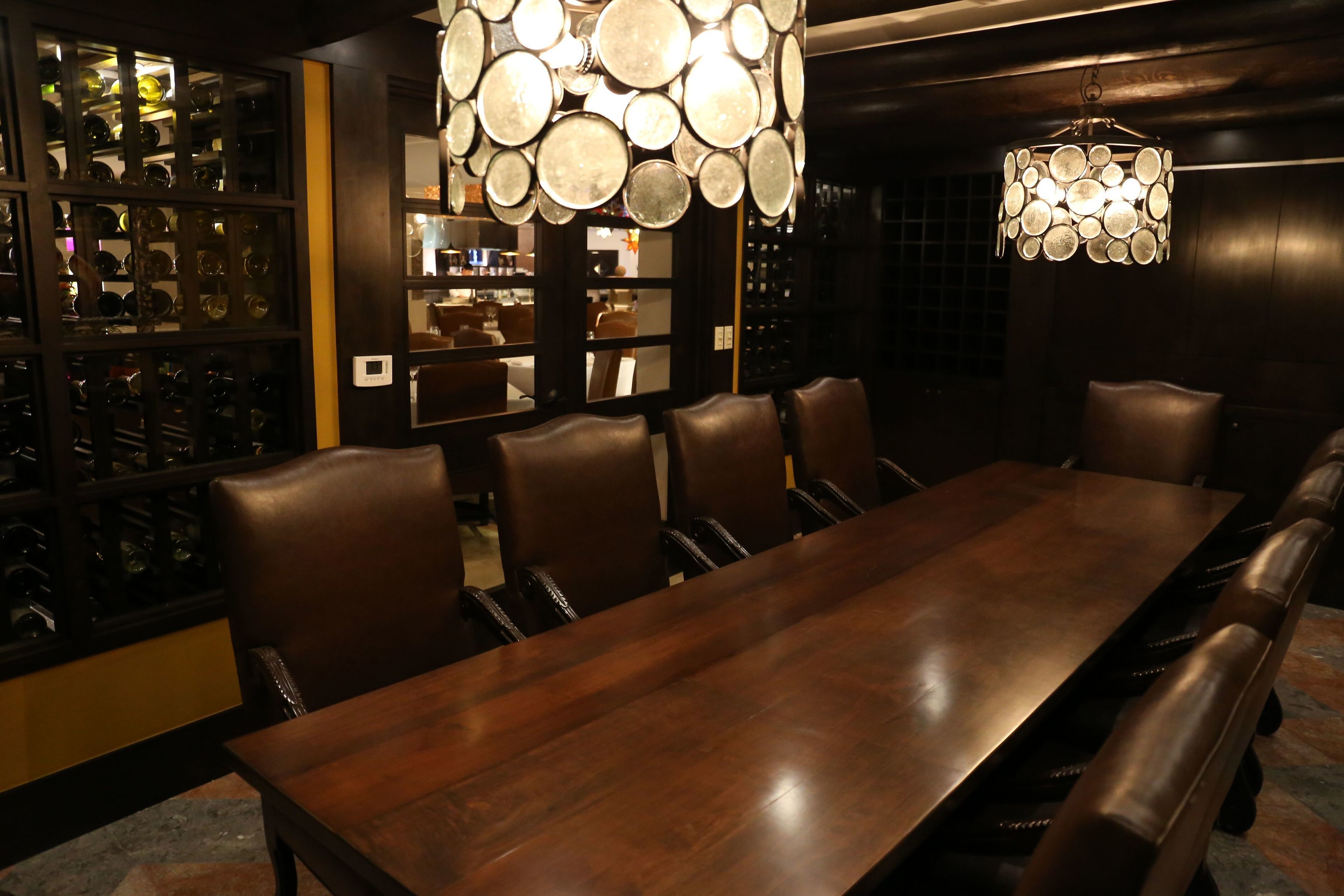 Comedor con una larga mesa de madera y sillas de cuero, rodeado de estanterías con cristalería.