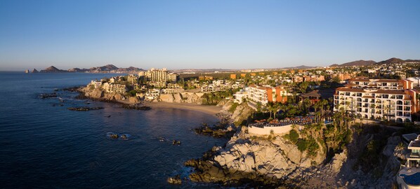 Un complejo turístico frente al mar con varias edificaciones, una playa y terreno rocoso.