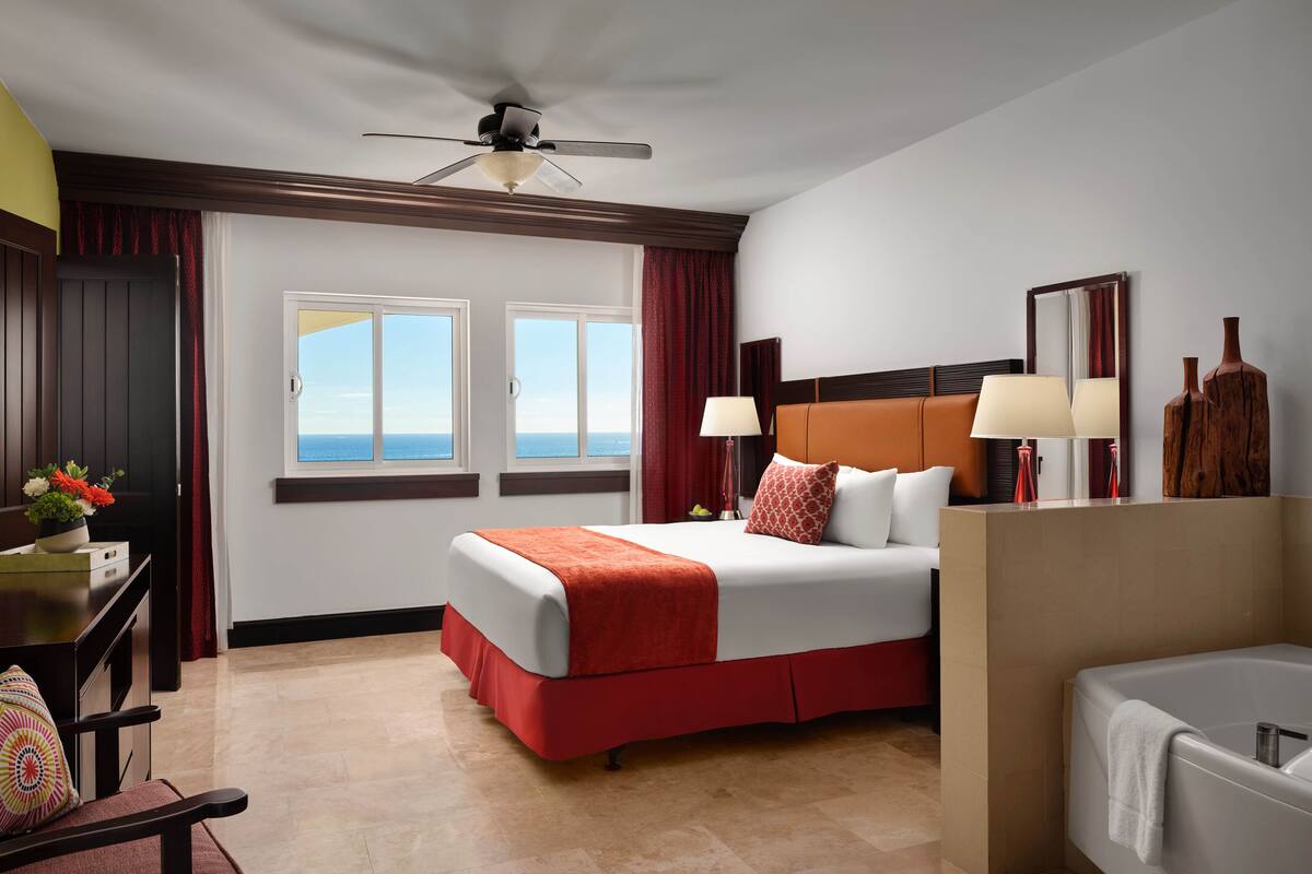 Quarto de hotel com cama, escrivaninha, cadeira, ventilador de teto, janela com vista e banheira.