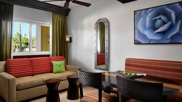 A modern living room with a sofa, a dining table, chairs, a ceiling fan, a large mirror, and a framed picture on the wall.
