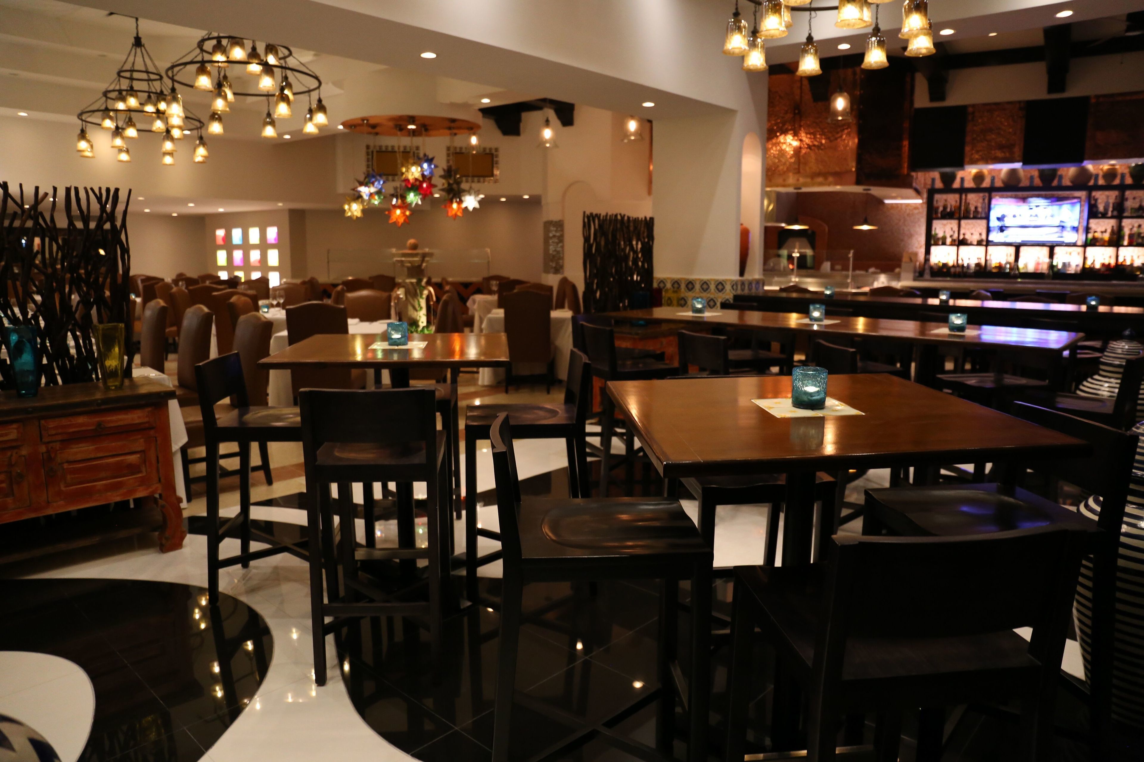 A restaurant with multiple tables and chairs, a bar area, and hanging light fixtures.