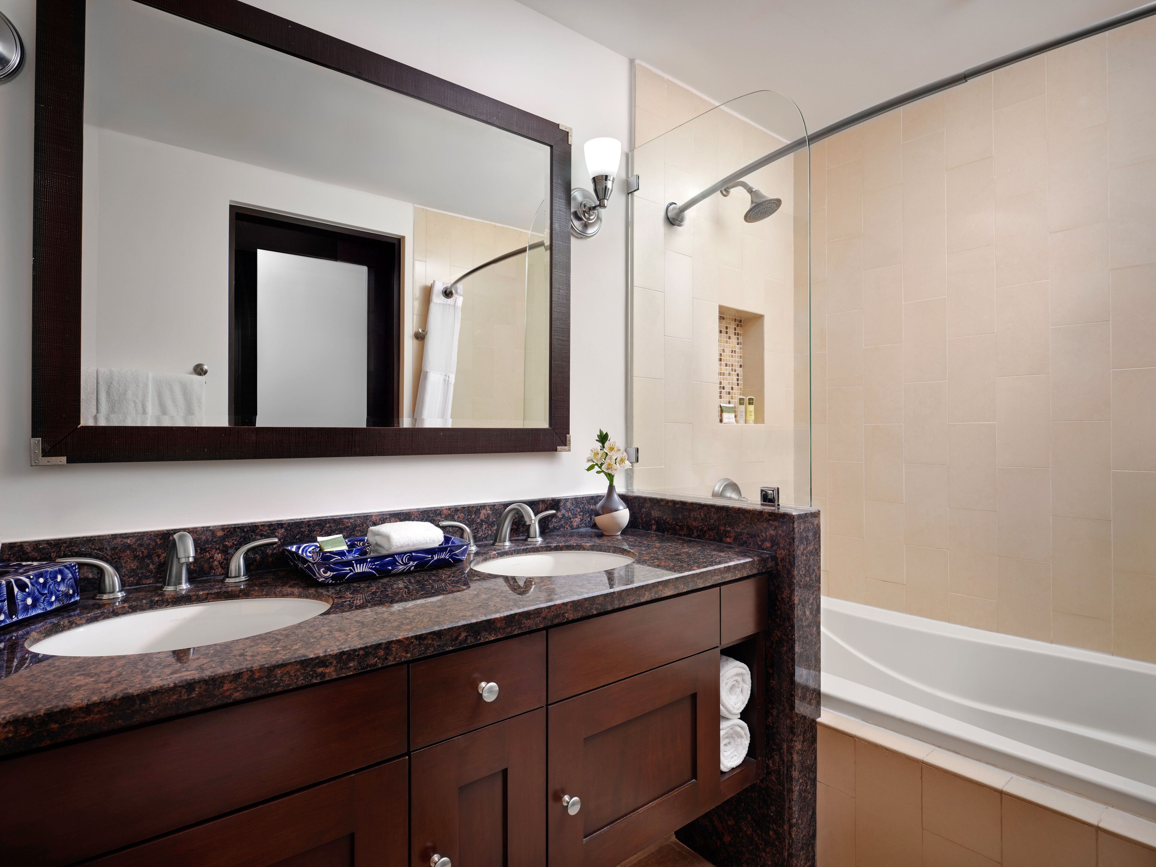 A modern bathroom with two sinks, a large mirror, and a glass-enclosed shower.