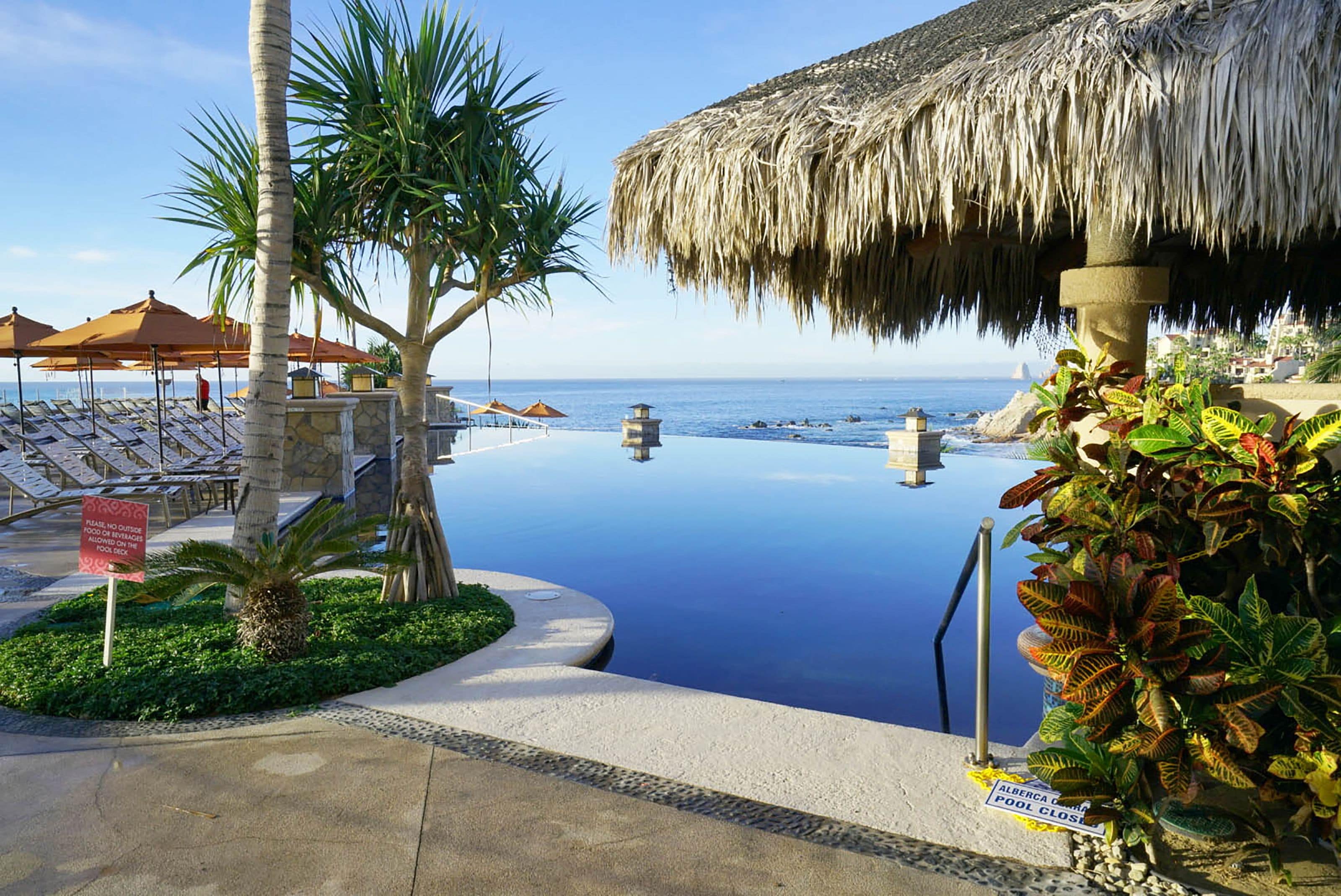 A poolside area with lounge chairs, a thatched umbrella, and a sign indicating the pool is closed.