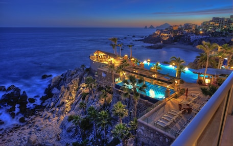 A beachfront hotel with a pool, palm trees, and a view of the ocean.