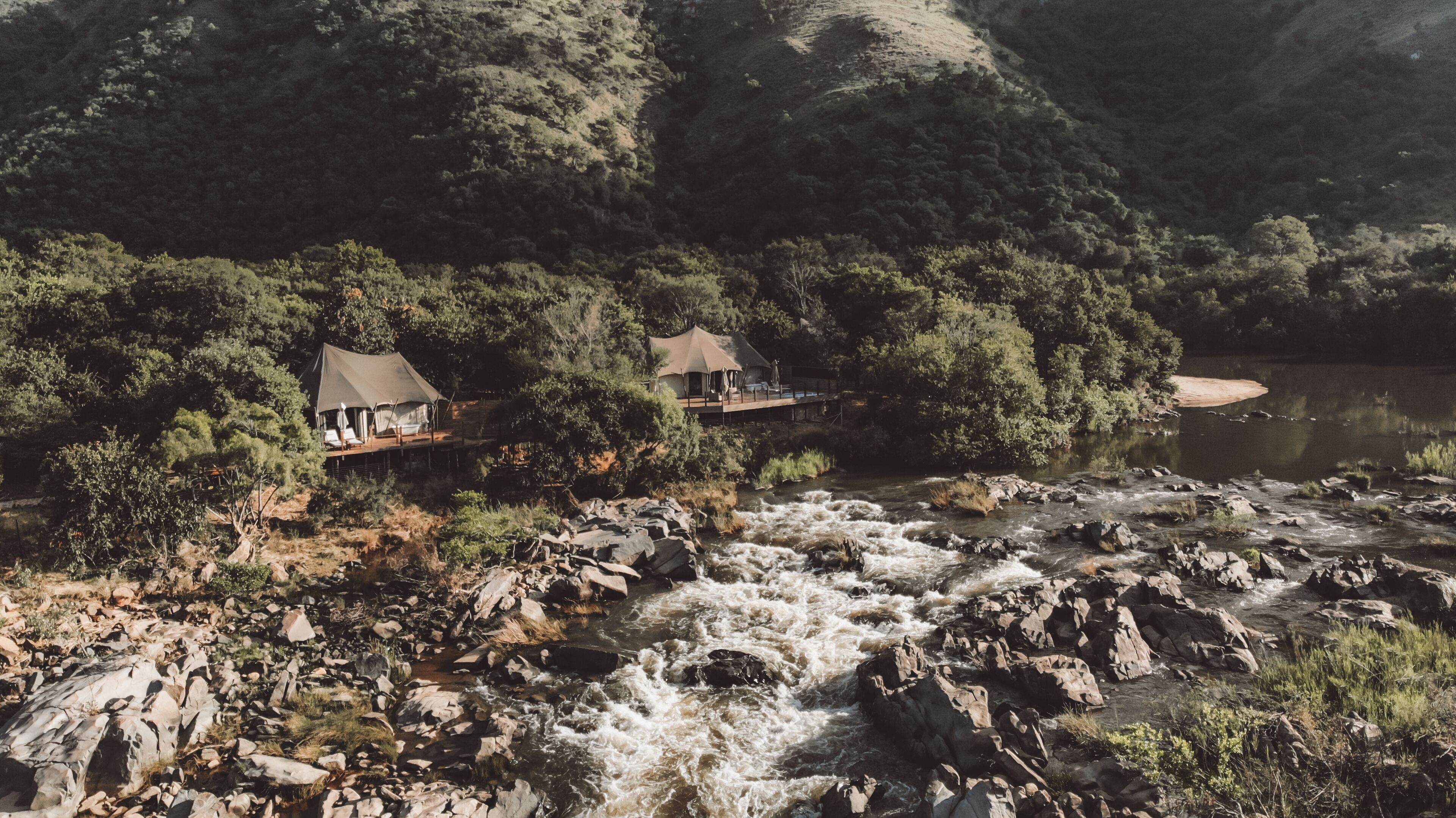 Ein Flussufer-Campingplatz mit zwei Zelten, felsigem Gelände und dichtem Wald.
