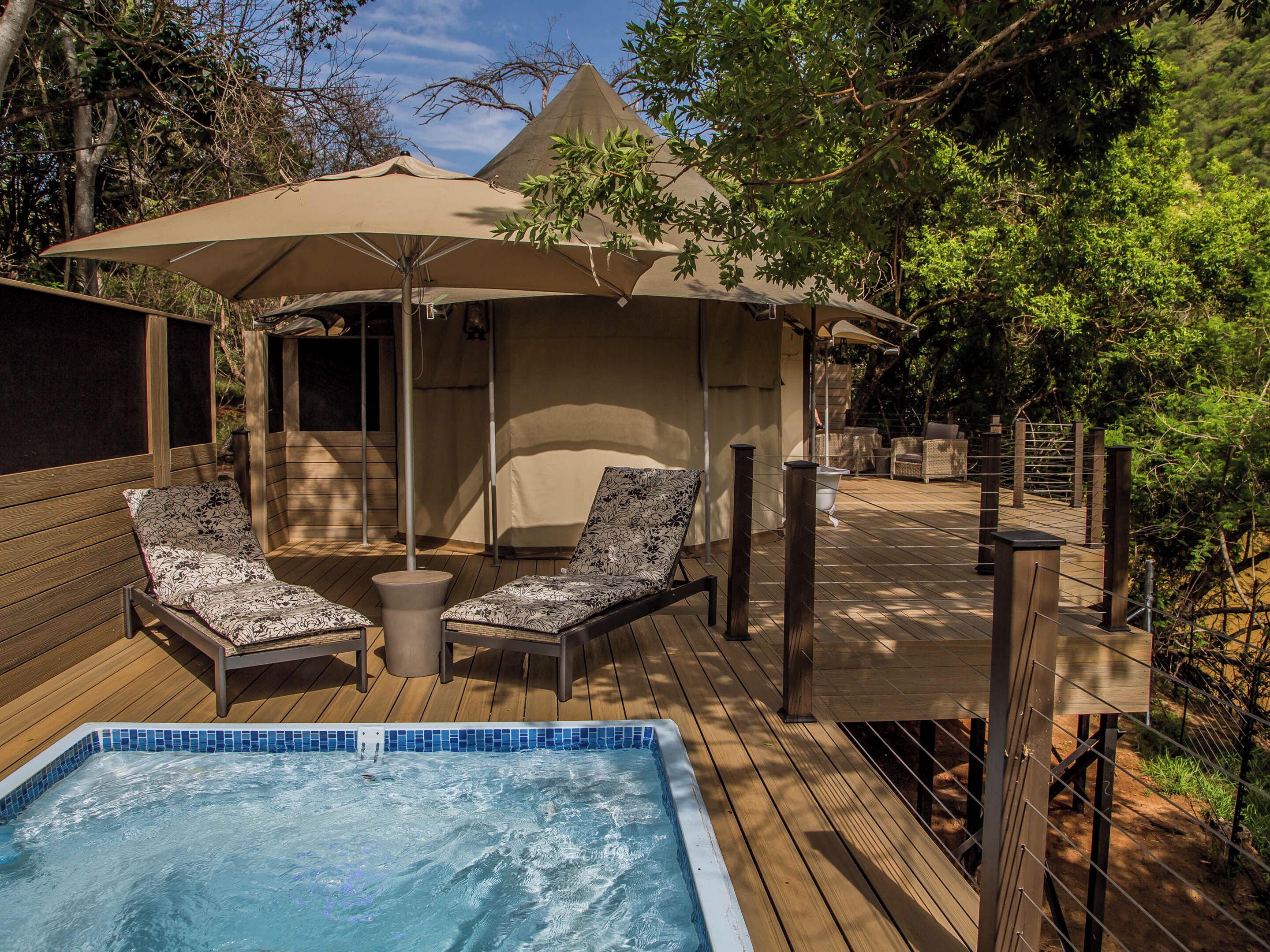 A wooden deck with a hot tub, lounge chairs, and a covered seating area with umbrellas.