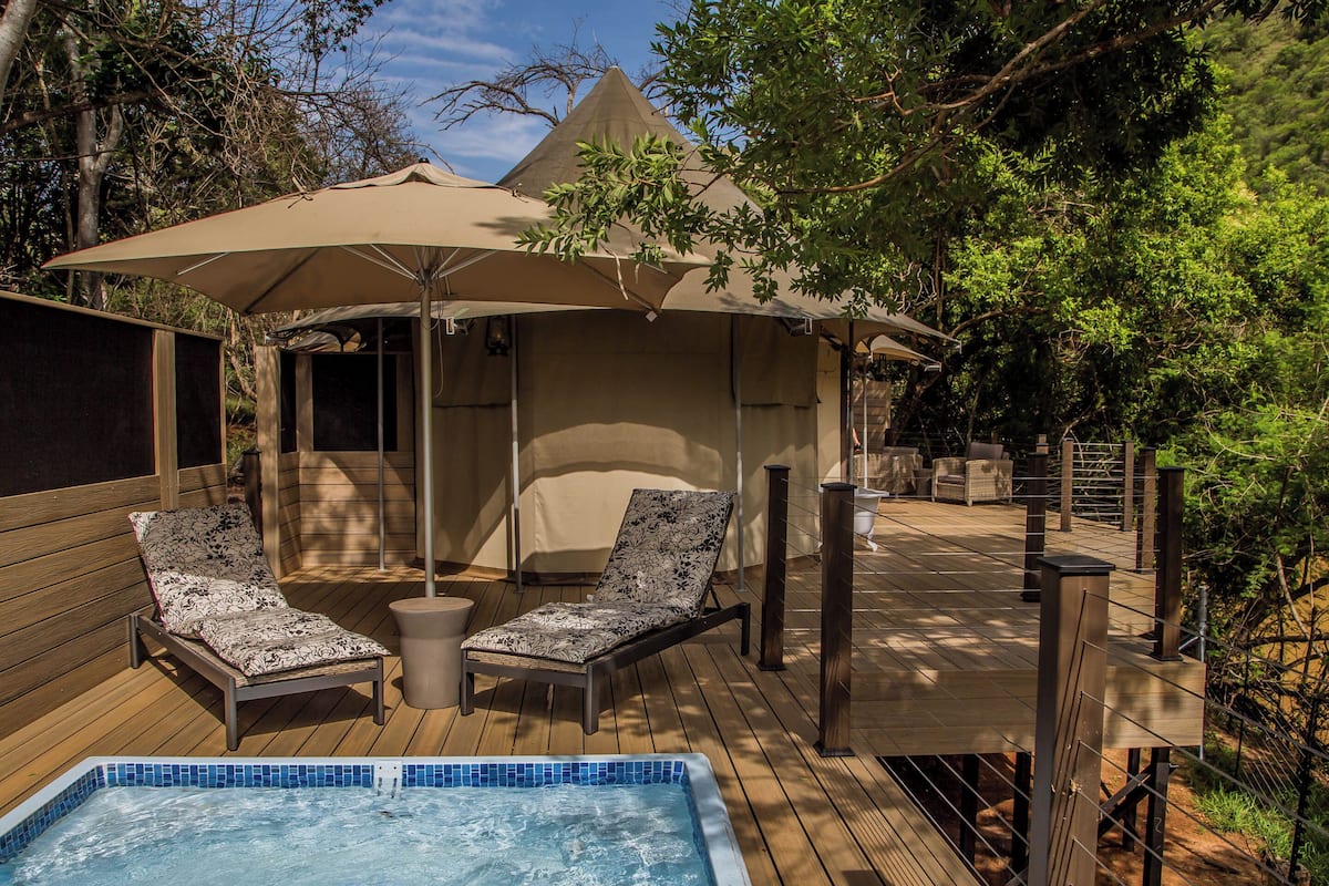 A wooden deck with a hot tub, lounge chairs, and a covered seating area with umbrellas.
