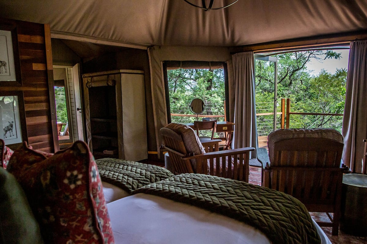 A tent-style room with a bed, two chairs, a table, and a view of the outdoors.