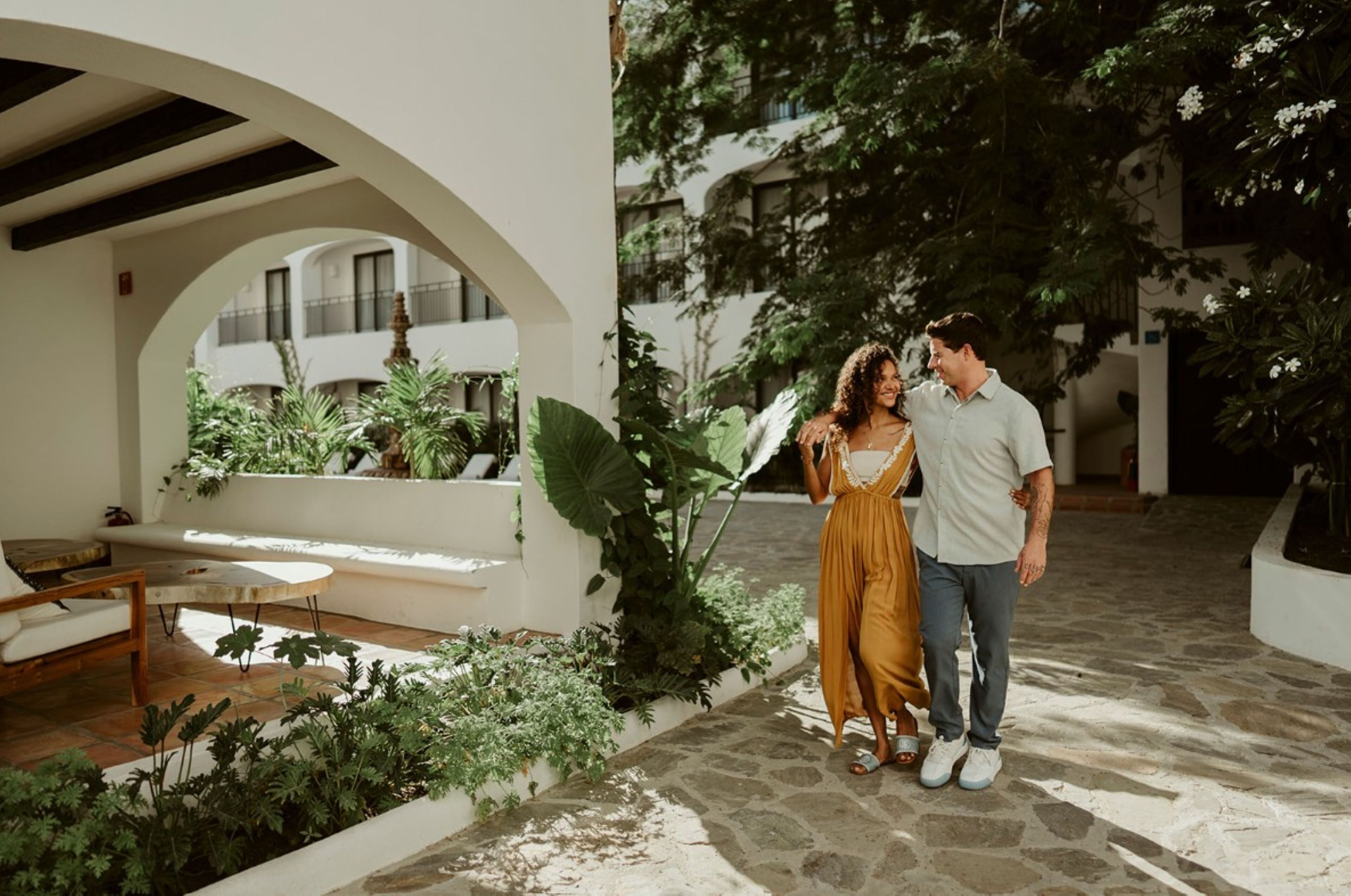 A courtyard with a white archway, a bench, and lush greenery.