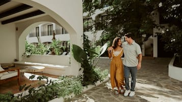 A courtyard with a white archway, a bench, and lush greenery.