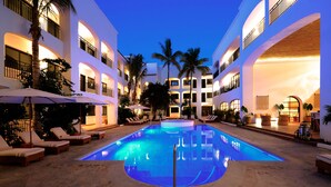 A pool area with lounge chairs and umbrellas, surrounded by multi-story buildings with balconies and palm trees. - Tropicana Los Cabos, Tapestry Collection by Hilton (San José del Cabo)
