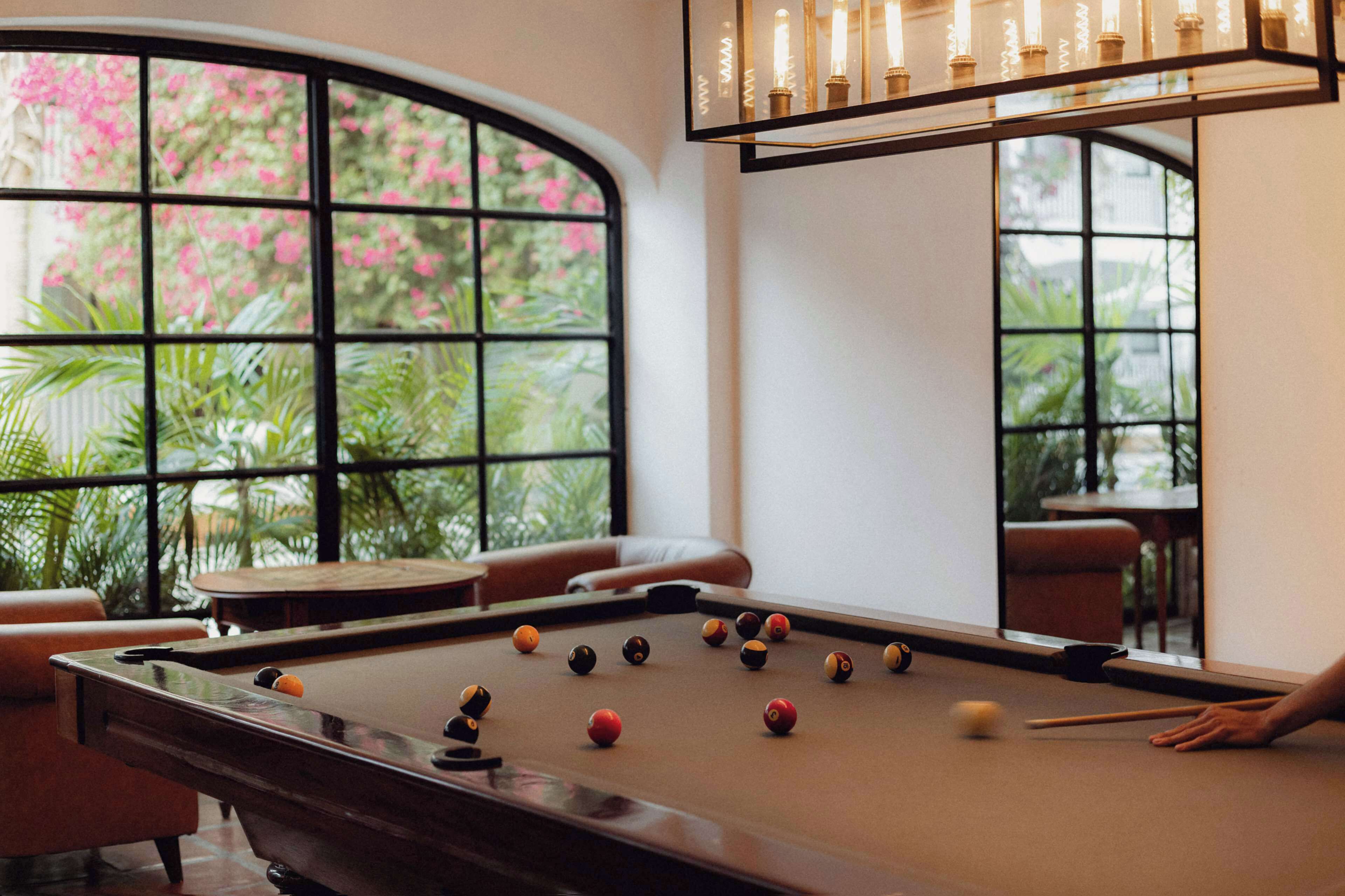 A pool table in a room with a curved window, a sofa, and a table with candles.