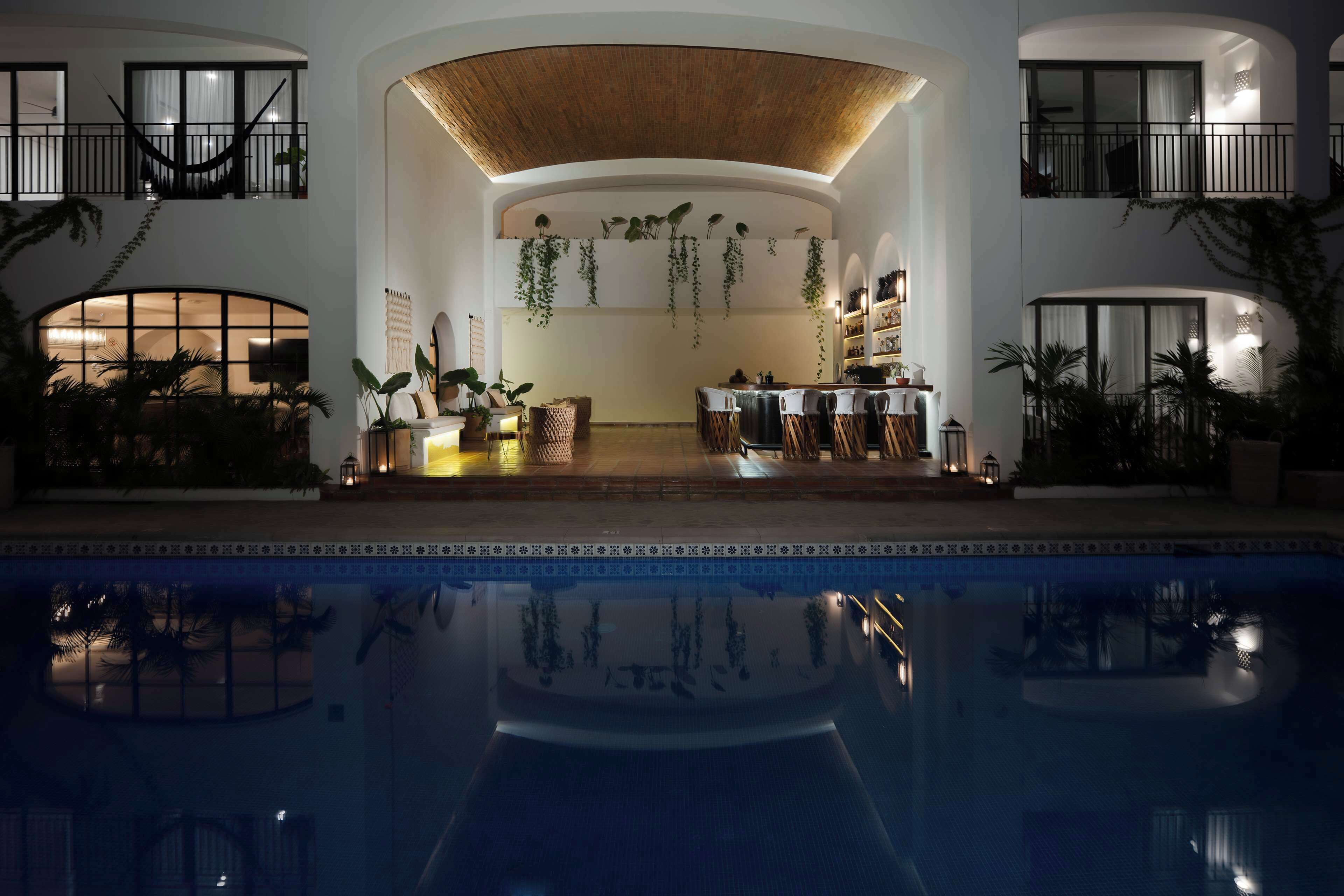 A poolside area with a dining setup, indoor plants, and a ceiling with hanging plants.