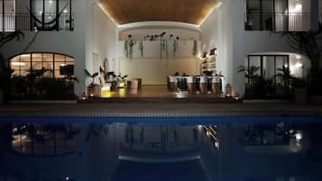 A poolside area with a dining setup, indoor plants, and a ceiling with hanging plants.