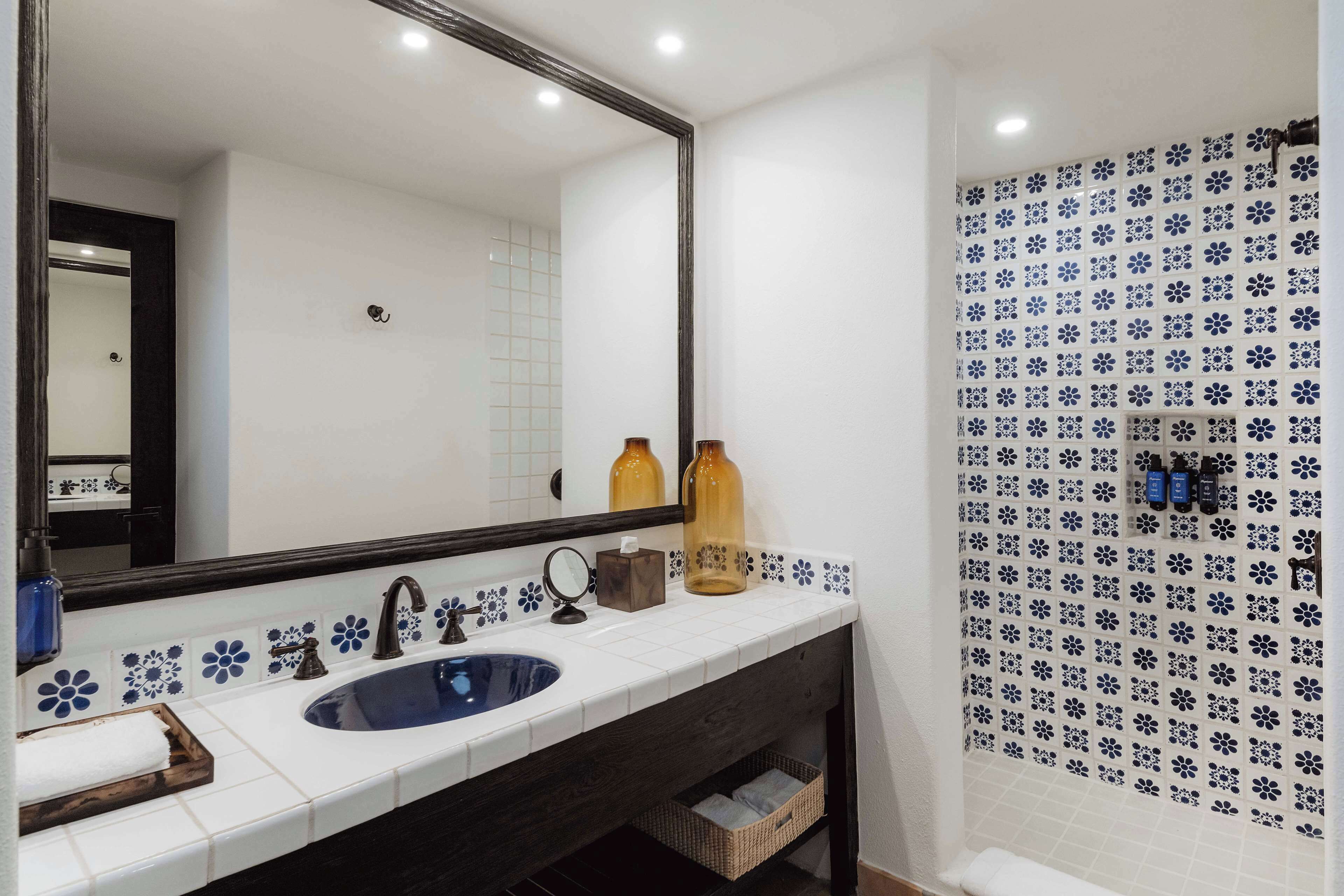 Une salle de bain avec un lavabo blanc, un meuble-lavabo en bois foncé et un miroir. On y trouve deux bouteilles sur le comptoir et un porte-serviettes.