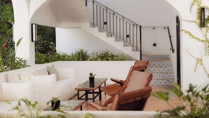 A modern outdoor living area with a white sofa, wooden chairs, a small table, and a staircase leading to an upper level. - Tropicana Los Cabos, Tapestry Collection by Hilton (San José del Cabo)
