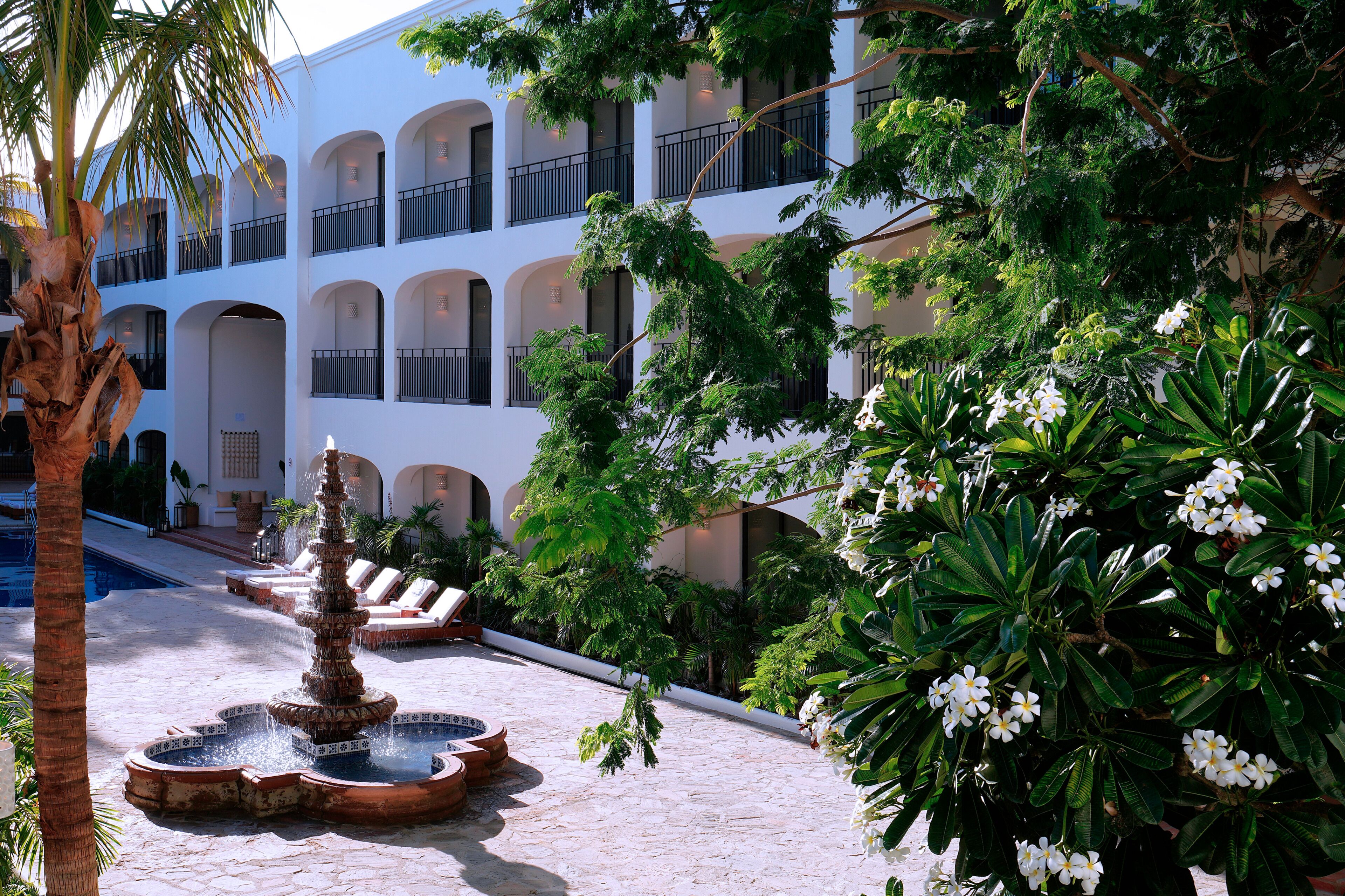 A courtyard with a fountain, palm trees, and a building with balconies.