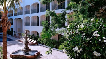 A courtyard with a fountain, palm trees, and a building with balconies.