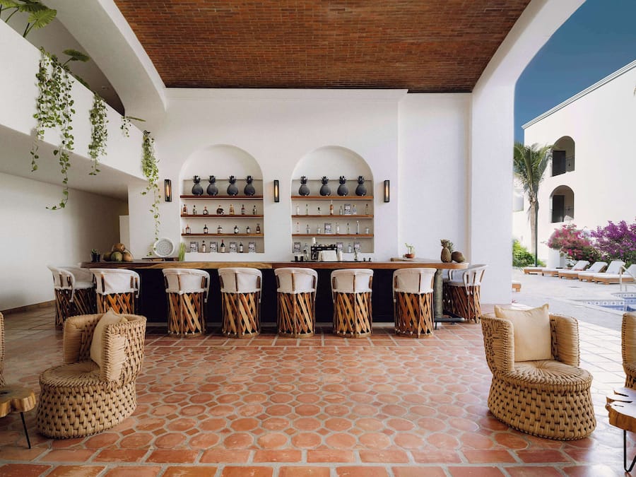 Uma área de bar com cadeiras de vime, piso de azulejos e prateleiras com garrafas.