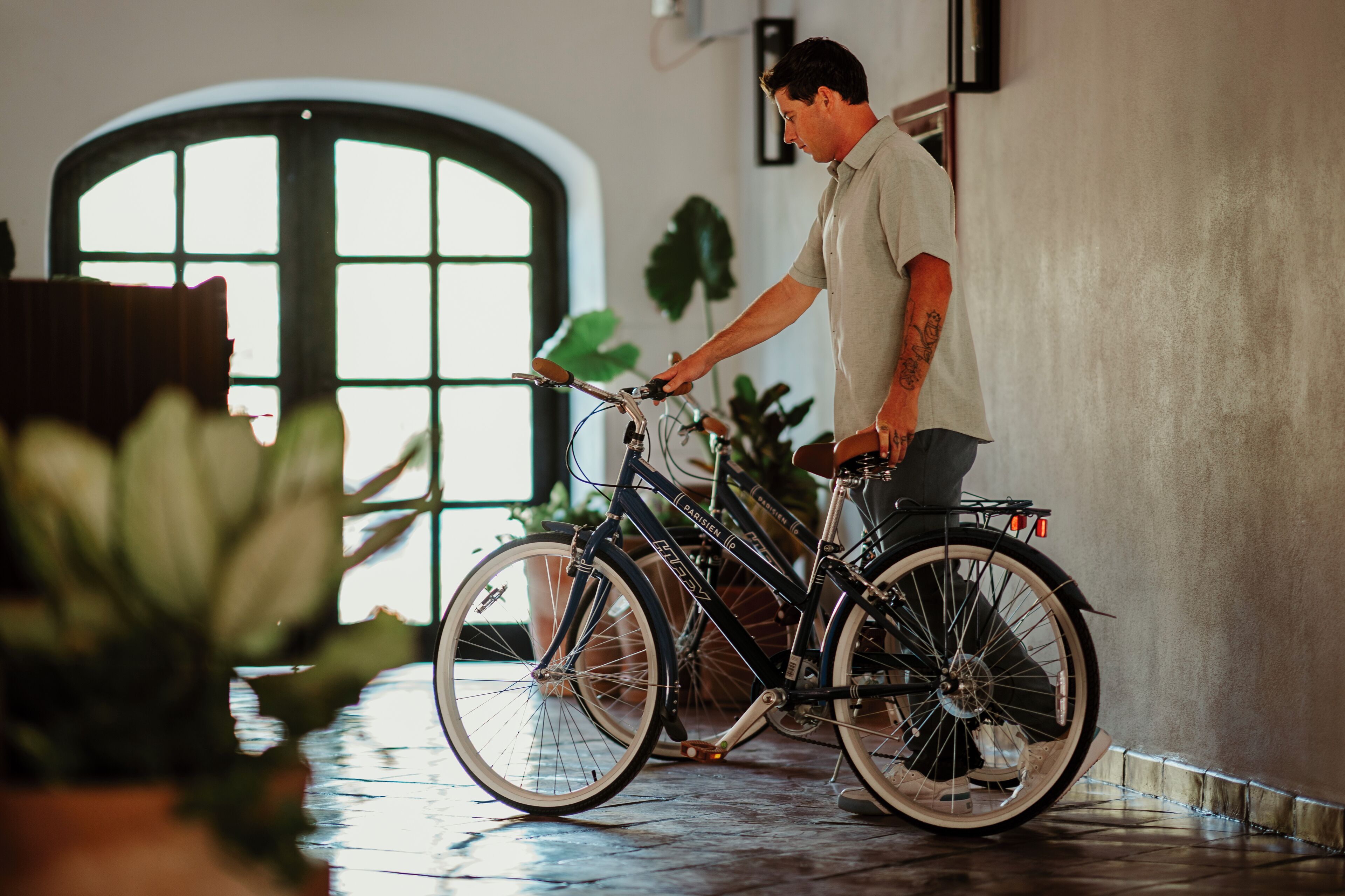 Un hombre en una bicicleta estática en una habitación con un ventanal grande y plantas en macetas.