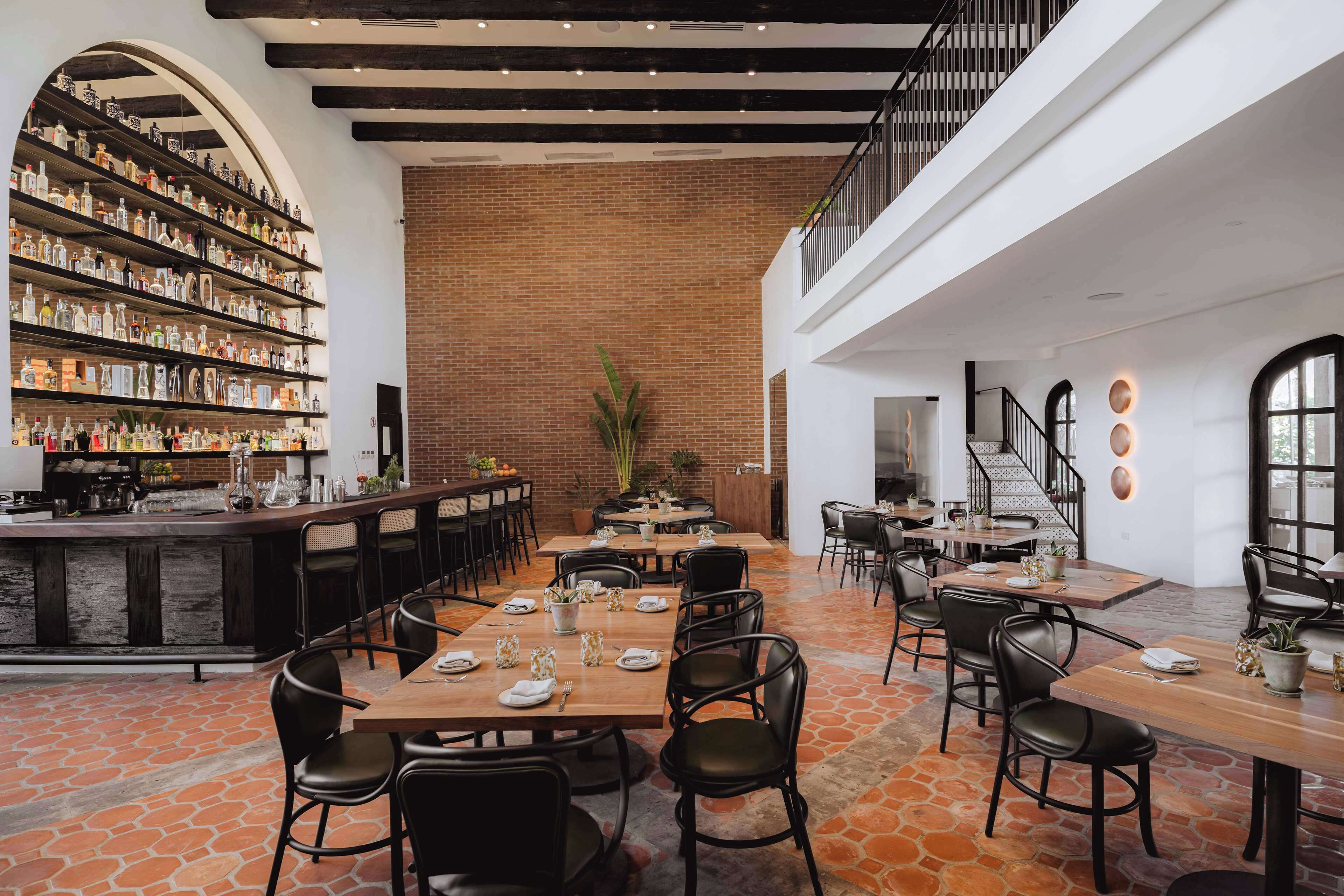 A spacious restaurant with a brick wall, wooden tables, and black chairs.