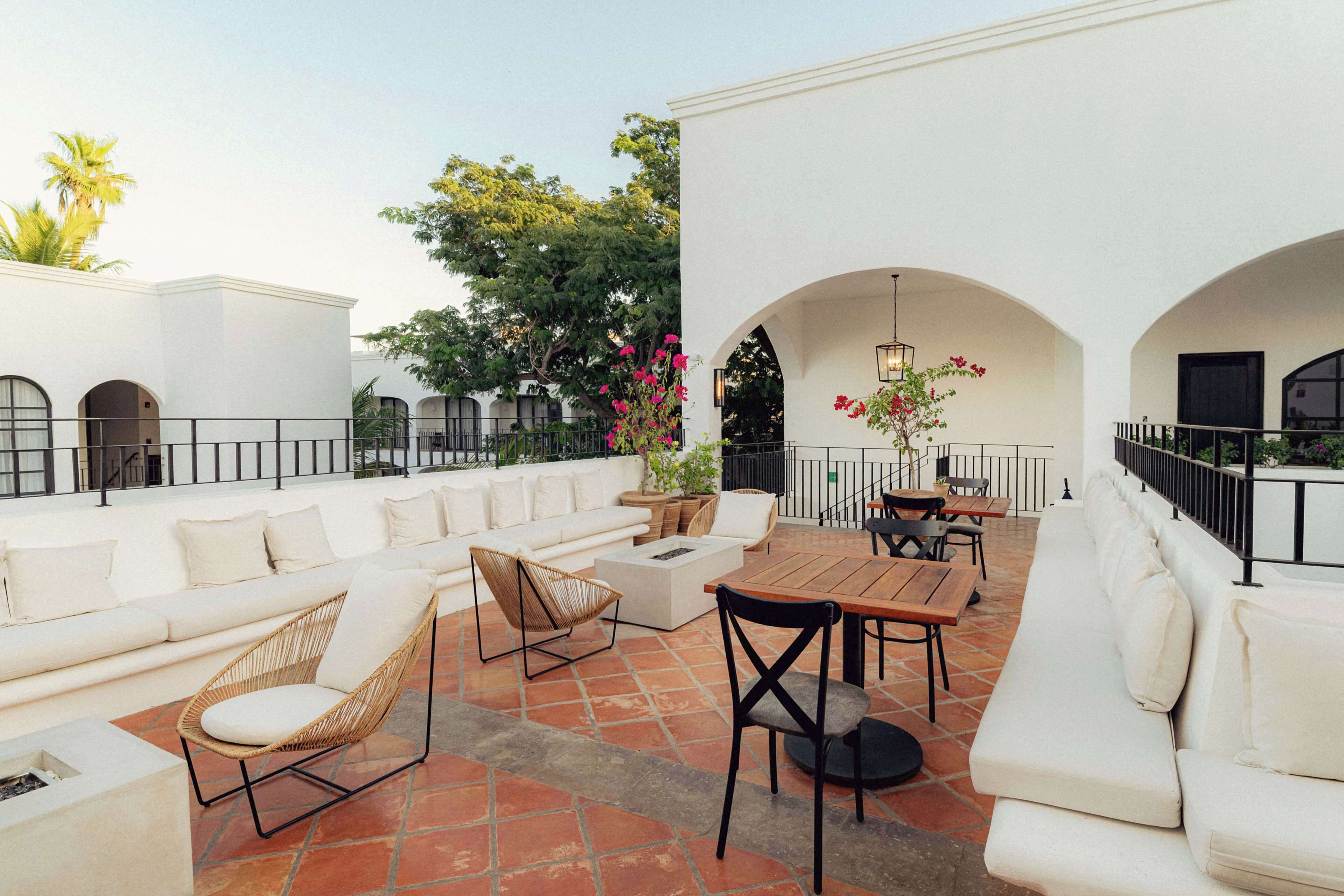 An outdoor patio with white sofas, wicker chairs, and a wooden table.
