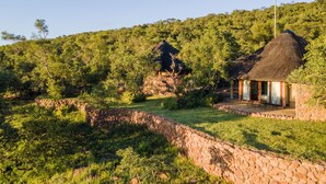 Een rustieke lodge met stenen muren en berghutten met rieten daken, verscholen in een weelderig groen bos.