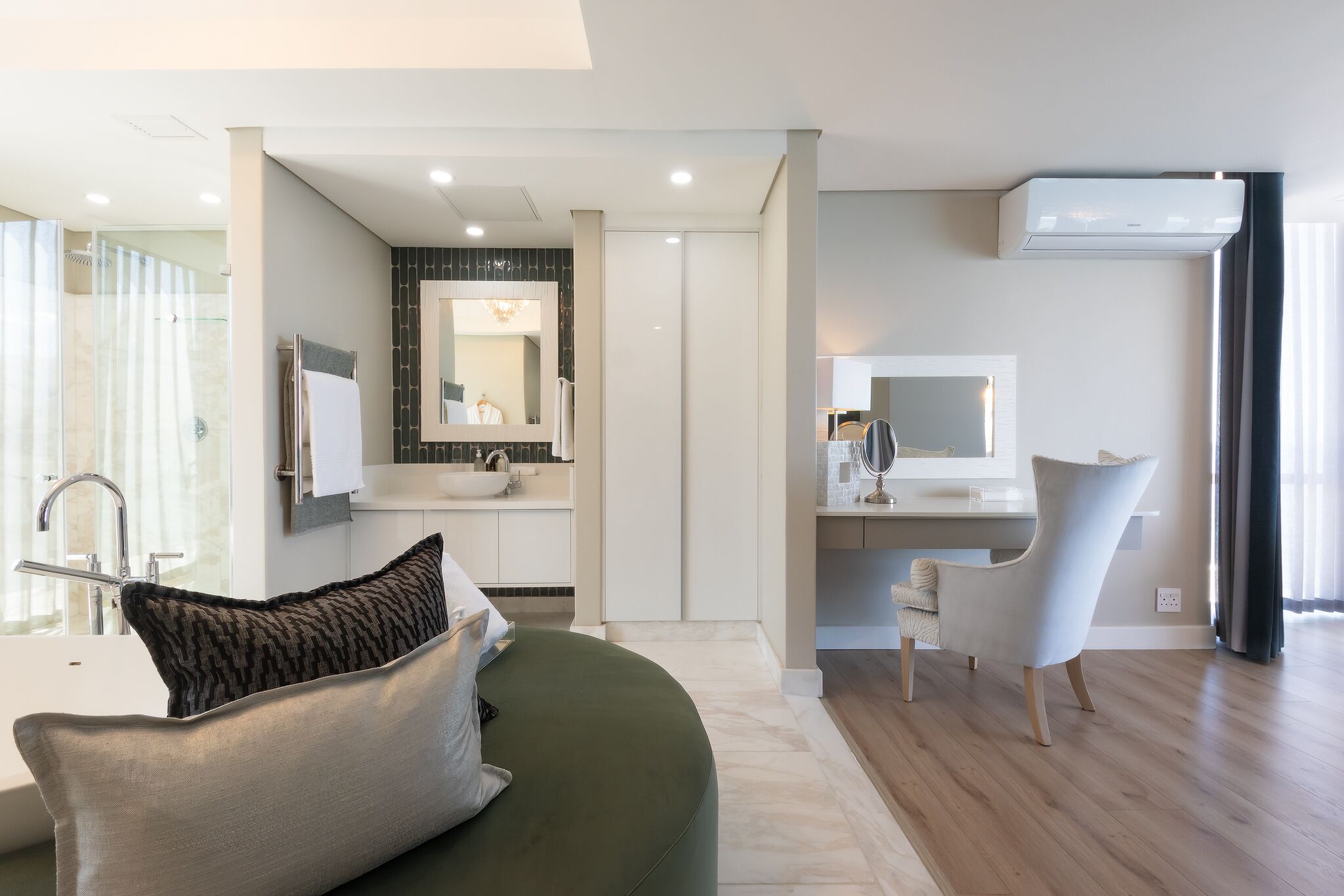 A modern bathroom with a shower, sink, and mirror. There is a green sofa with a pillow and a chair.