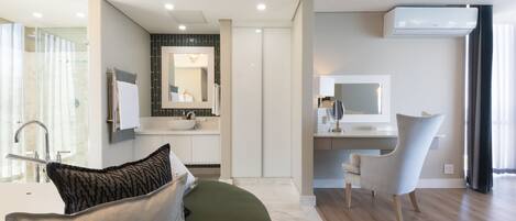 A modern bathroom with a shower, sink, and mirror. There is a green sofa with a pillow and a chair.