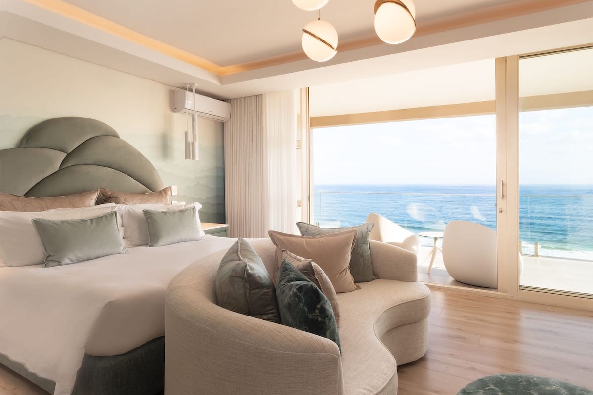 A modern bedroom with a curved sofa, a large bed, and a view of the ocean.