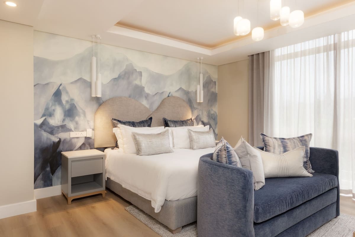 A modern bedroom with a bed, bedside tables, a sofa, and a mountain-themed wall mural.