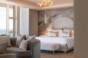 A modern bedroom with a large bed, a sofa, and a view of the sea.